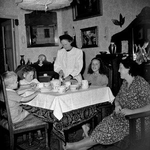 823249 Afbeelding van een Zuster Augustinesse die het brood snijdt aan tafel bij een gezin in Wijk C te Utrecht; de ...